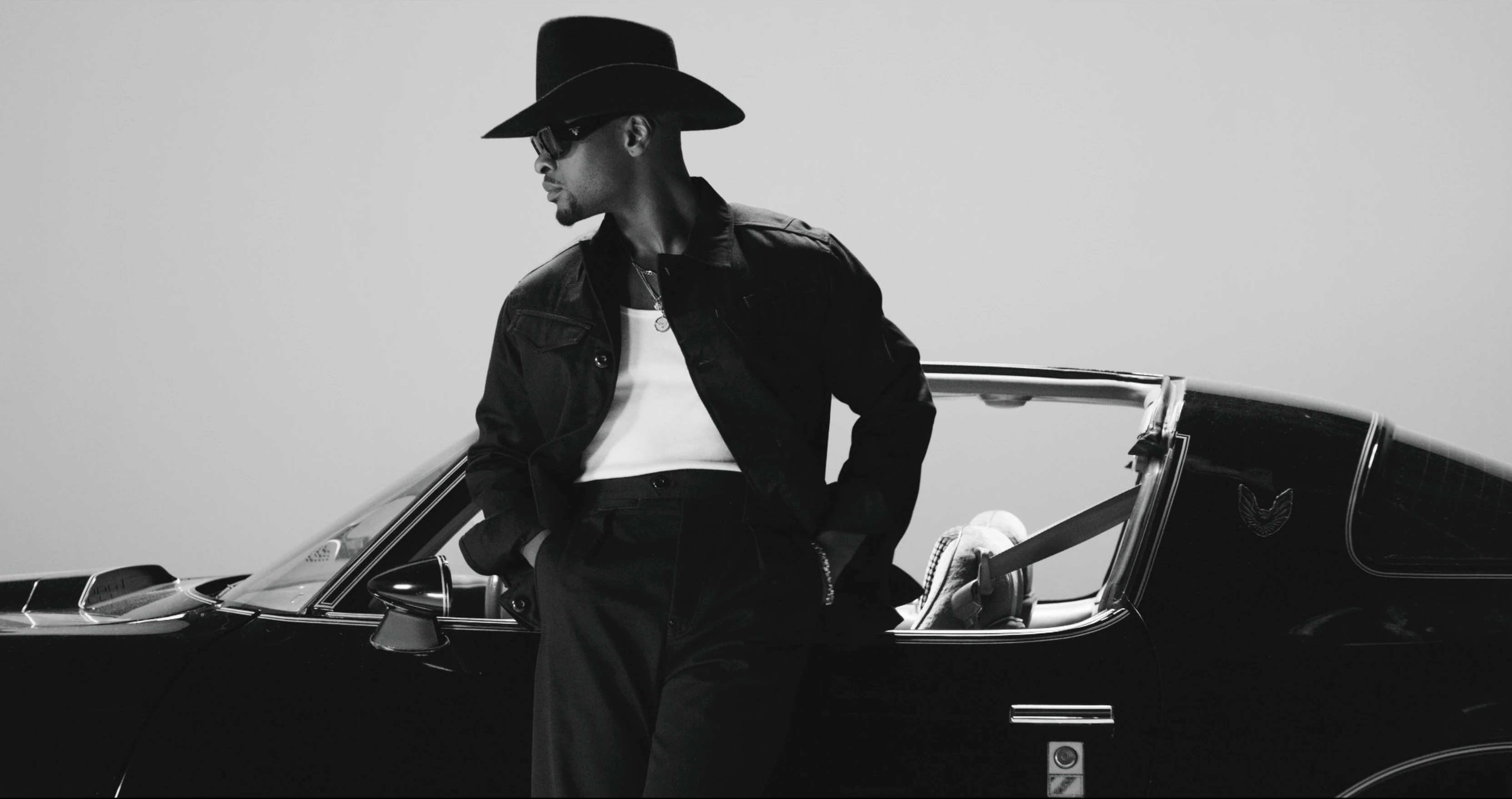 Man in a wide-brim hat leaning against a black Trans Am
